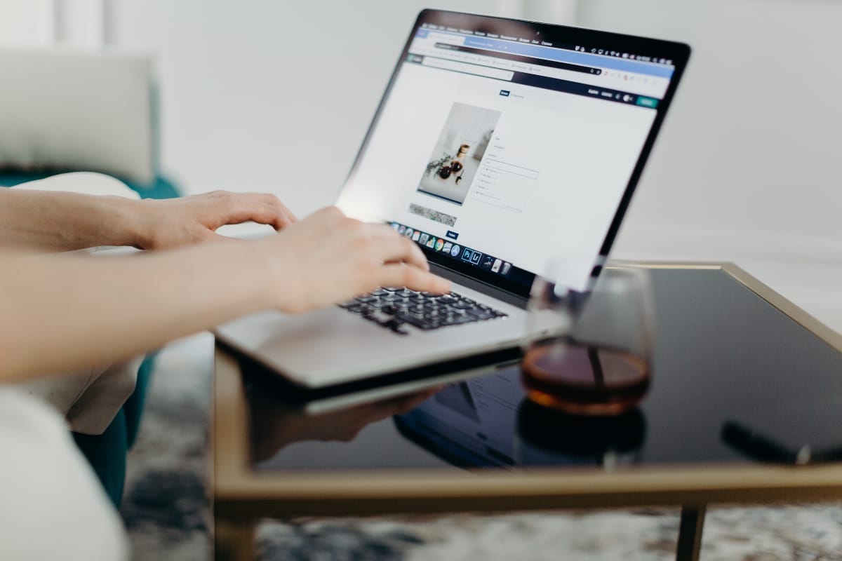 A person intently types on a laptop, perched on a glass-topped table beside a refreshing glass of liquid. The screen showcases a secure web page, its SSL certificate ensuring data protection.