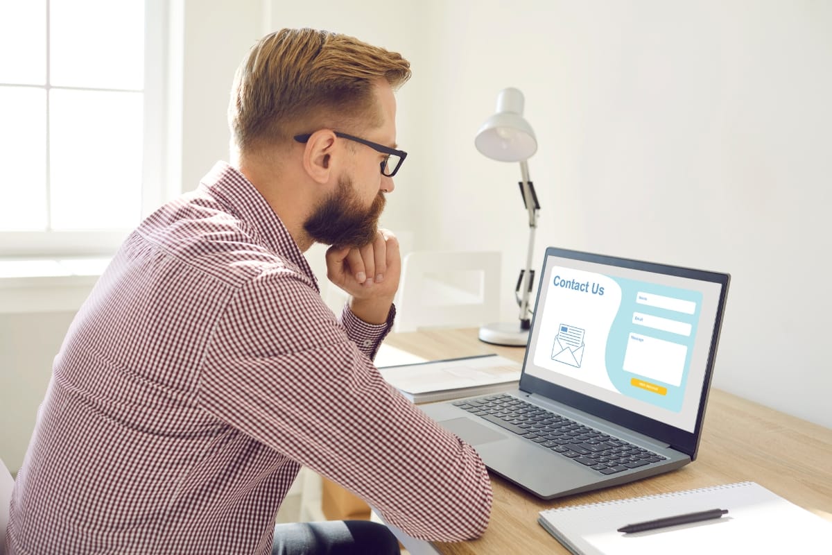 A man in glasses peers intently at his laptop, where a "Contact Us" form is prominently displayed. The screen's reassuring lock icon signifies the presence of an SSL certificate, ensuring secure communication.