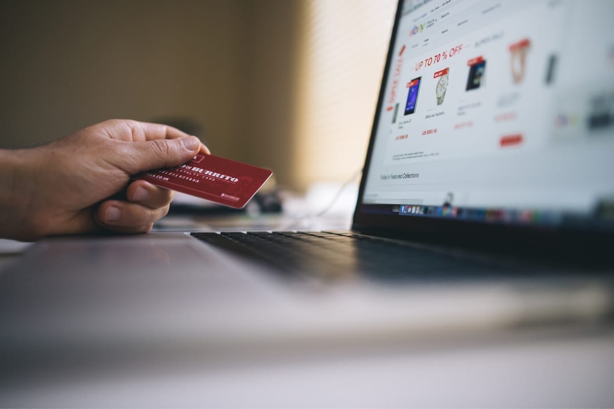 A person holds a red debit card in front of an open laptop displaying an online shopping site, where the presence of an SSL certificate ensures secure transactions.