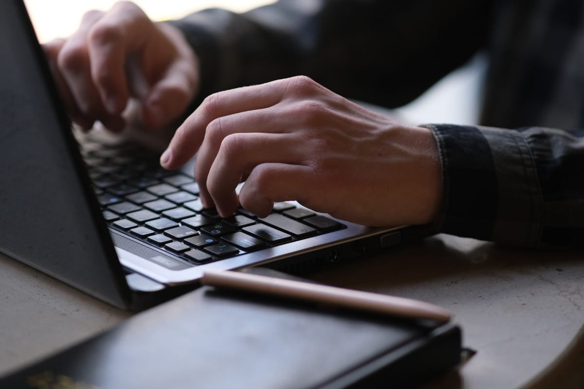 Hands typing on a laptop keyboard, working diligently on a WordPress backup, with a notebook and pen nearby.