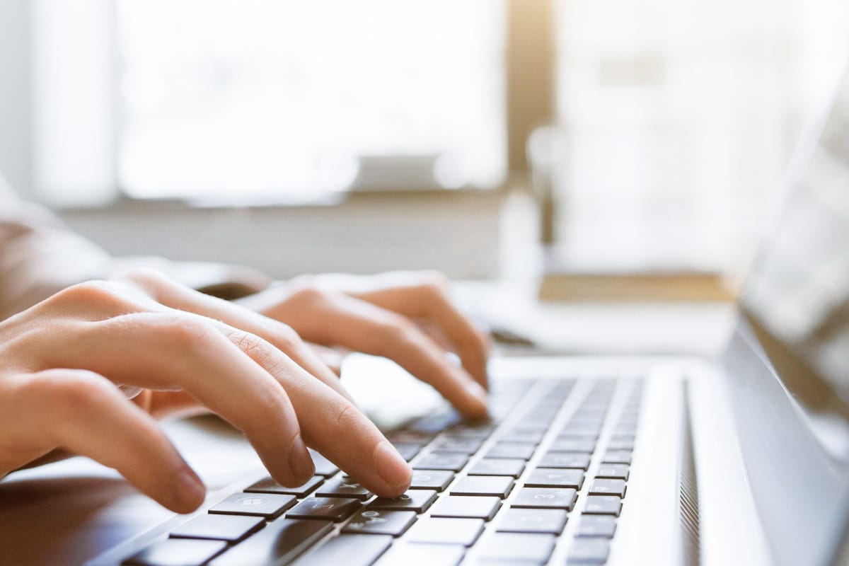 Hands typing on a laptop keyboard in a bright, sunlit room, expertly navigating WordPress user role management.