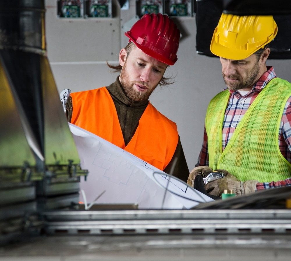 Two construction workers analyzing HVAC blueprints in a factory.