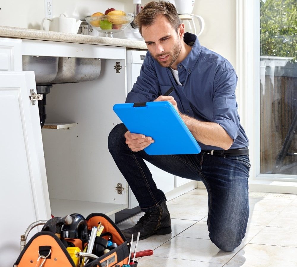 A plumber inspecting a sink with a clipboard.