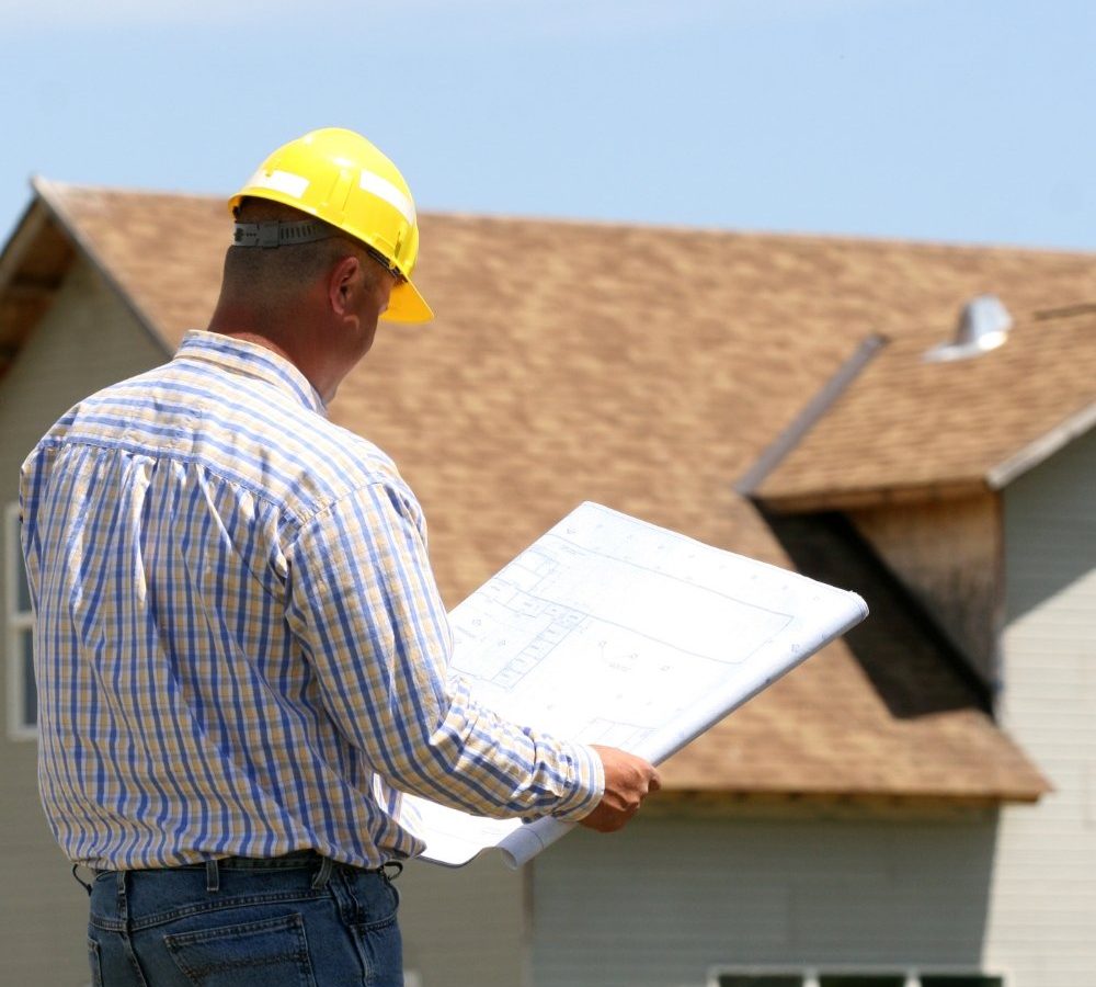 A man utilizing a blueprint to showcase roofing marketing strategies in front of a house.