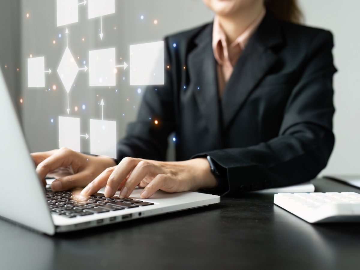 Person in a suit working on a laptop with floating digital flowchart icons above the keyboard, focusing intently on sales pipeline management.