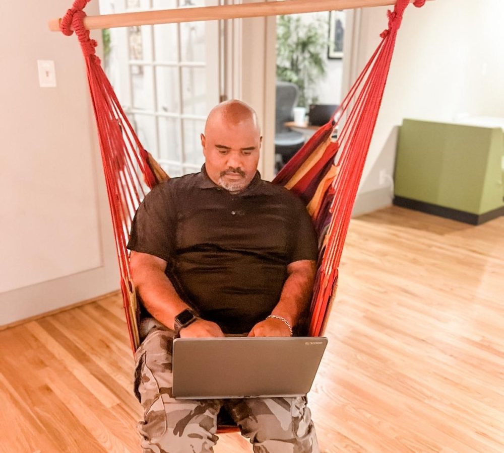 A man in a hammock chair engaging in content writing on his laptop.