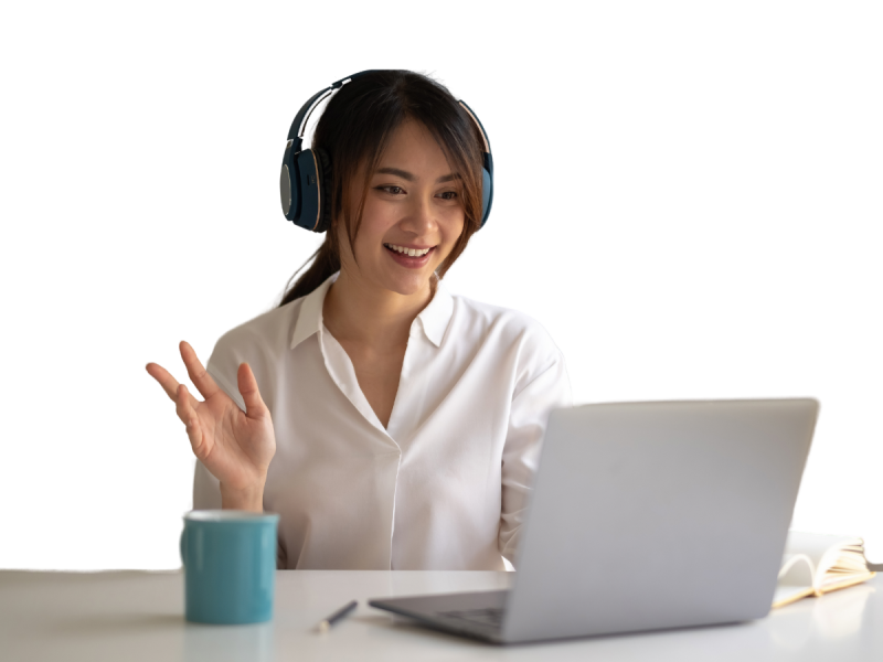 A woman wearing headphones sits at a desk with a mug and a laptop, smiling and waving at the screen, likely discussing business automation strategies for her small business CRM.